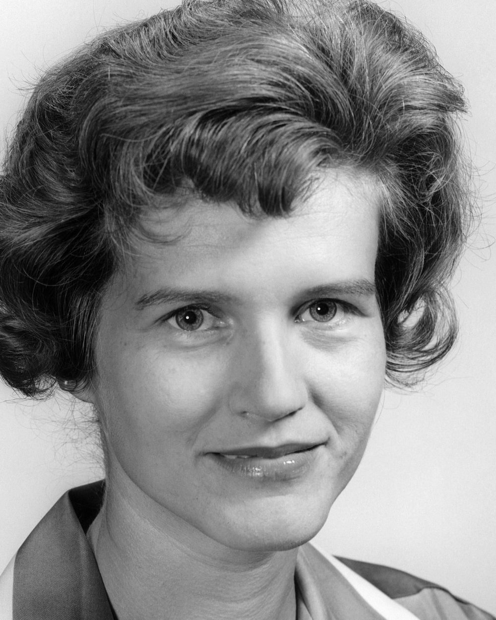 A black and white 1960s studio portrait of a smiling woman.